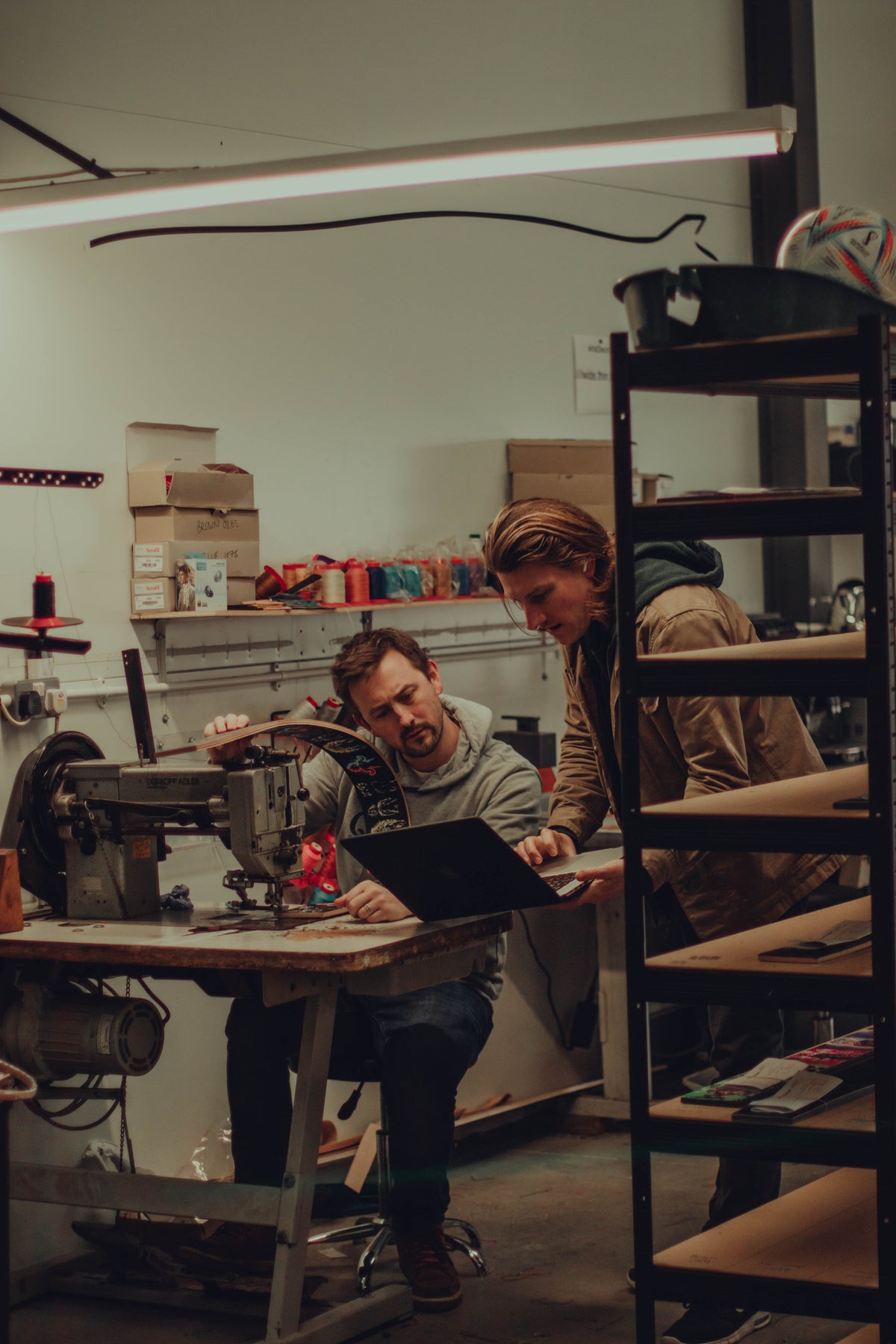 Reviewing a belt and a laptop beside a sewing machine in the workshop