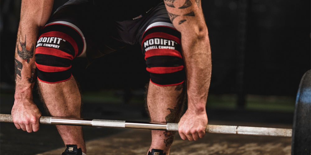 Lifter wearing red and black ModiFit knee sleeves at a barbell
